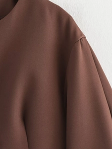 Detail view of the brown cropped jacket showing crew neck and subtle shoulder pleats