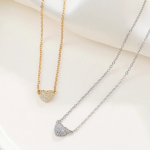 Close-up of gold and silver heart necklaces with micro-paved zircons on white silk fabric