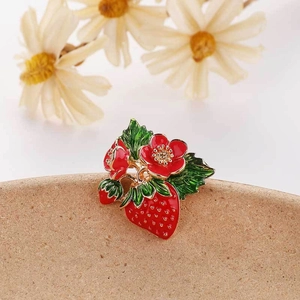 Macro detail of red enamel strawberry brooch with green leaves and golden metallic dots