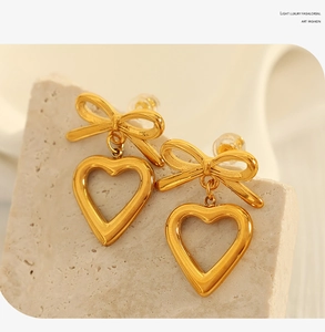 Close-up of golden bow and heart pendant earrings on a textured stone surface