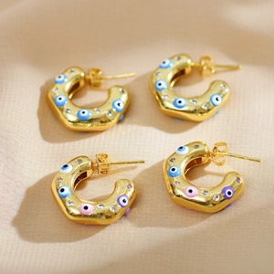Detail of C-shaped gold earrings with colorful evil eye charms and tiny zircons