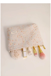 Detailed view of beige tweed cosmetic bag with zipper and elegant makeup accessories