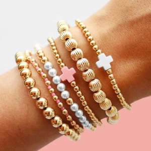 Close-up of stacked gold bead bracelets and white faux pearls on female wrist