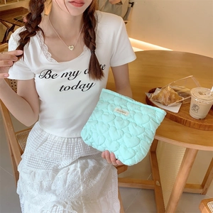 Detail of mint green quilted makeup bag with heart pattern held in a cafe setting