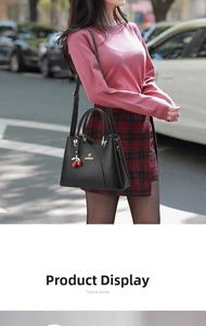 Close-up of black lychee leather handbag with red cherry charm and golden logo