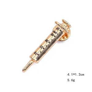 Detail of a golden syringe brooch with black scale markings and a butterfly clasp back