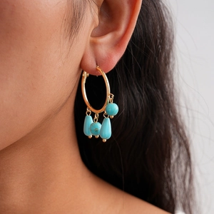 Close-up of bohemian gold hoop earrings with turquoise teardrop tassels on model