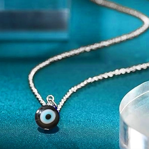 Close-up of a silver stainless steel chain with a glass-like blue evil eye amulet pendant