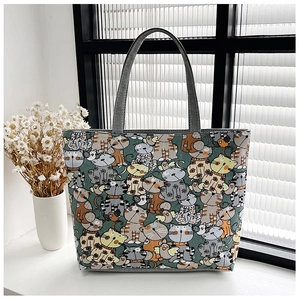 Close-up of a green canvas tote bag featuring playful cartoon cat prints and grey handles