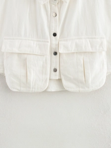 Detailed macro view of white denim vest featuring silver metal buttons and flap pockets