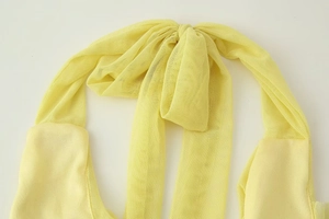 Macro view of a yellow mesh halter neck dress showing fabric texture and tie detail