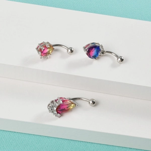 Three gradient crystal heart belly button rings displayed on a clean white pedestal stand