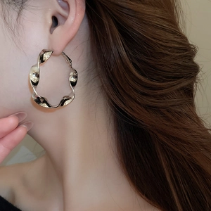 Gros plan d'une boucle d'oreille créole torsadée dorée portée par un mannequin