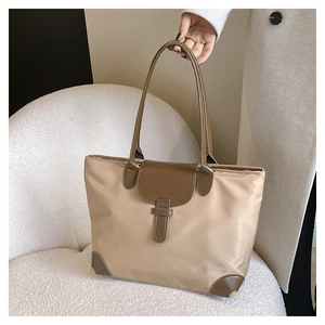 Detail of khaki nylon tote bag with brown leather corners shown on a cozy white armchair
