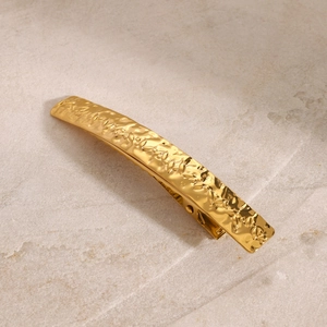 Golden stainless steel hair clip with leaf relief texture on a beige stone background