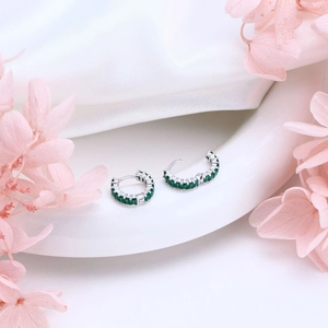 Macro detail of S925 silver hoop earrings with green zircon tassels on silk backdrop