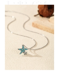 Macro shot of silver starfish pendant with turquoise stone and zircon on sand background