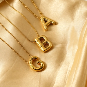 Close-up of golden balloon style alphabet pendants on diverse gold chains over silk