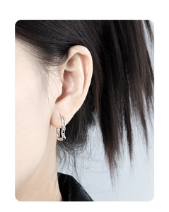 Macro detail of irregular U-shaped silver earring with white diamonds on a female model