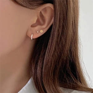 Close-up of three layered 925 sterling silver earrings featuring a golden smiley face stud