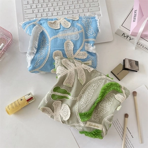 Detail of floral embroidery and fringe on cotton makeup bags in blue and green