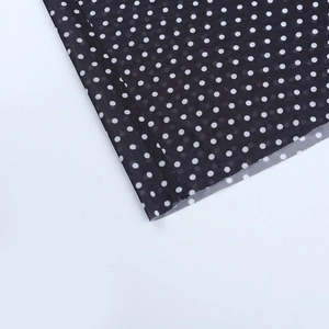 Close-up of semi-transparent black mesh fabric with white polka dots and stitched hemline