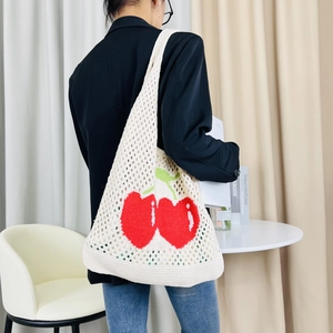 Close-up of a white knit tote bag with red cherry pattern worn by a model in a suit