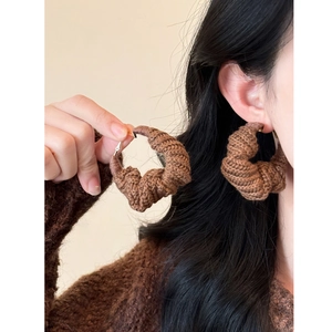 Gros plan de créoles en laine tricotée main marron sur un mannequin pour un look rétro