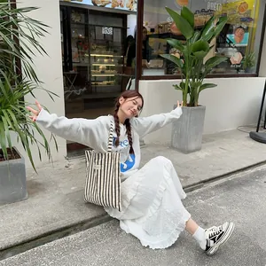 Outdoor street shot of striped canvas tote bag with white sweatshirt and tiered skirt