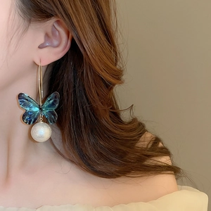 Detail of elegant butterfly earrings with blue gradient wings and round pearl drop