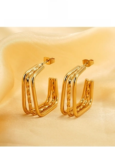 Macro shot of multi-layer titanium steel square hoop earrings on gold silk background