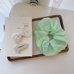 Detailed set of light green organza scrunchie and cream lace hair clips on a white tray
