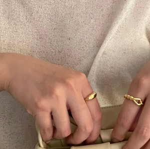 Detail of gold water-drop ring and twisted band set styled with a woven clutch