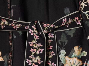Détail de la ceinture à nouer fleurie sur une robe noire soyeuse aux motifs colorés
