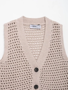 Detailed macro view of beige crochet knit vest showing fine hollow textures and dark buttons