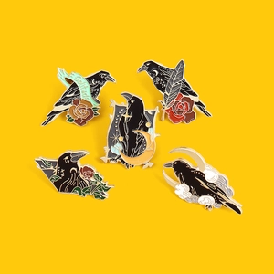 Gothic style crow enamel pins set with moon and rose elements on yellow background