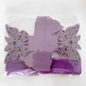 Detailed view of laser-cut purple butterfly favor boxes with silk ribbons in packaging
