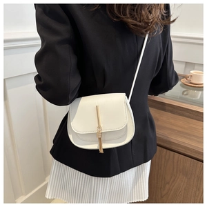 Detail of a white small saddle bag with gold tassel decor and stylish faux leather texture