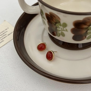 Elegant oval red agate stud earrings with gold plating displayed on vintage porcelain