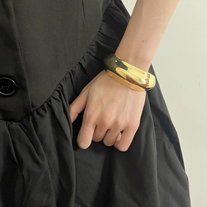Close-up of a wide polished gold metal double-layer cuff bracelet on a model's wrist