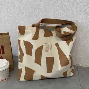 Detail of canvas tote bag featuring an abstract rabbit reading print and brown handles