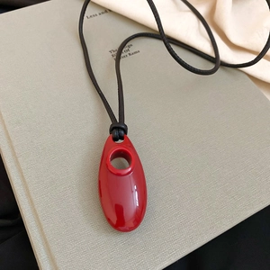 Close-up of bright red oval lacquer pendant on black cord over a textured book background