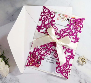 Detail of laser-cut glitter dark pink invitation cover with beige satin ribbon and floral card