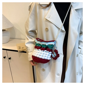 Detailed close-up of a handmade knit bucket bag with pearl strap and cherry red accents