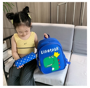Blue kids dinosaur backpack set with matching pencil case shown with a child on a sofa