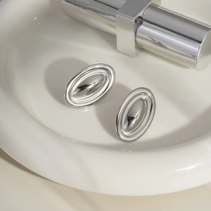 Close-up of minimalist oval mirror-polished earrings resting on a white ceramic tray