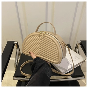 Dettaglio borsa beige a mezzaluna con trapuntatura a V e cerniera dorata su una sedia