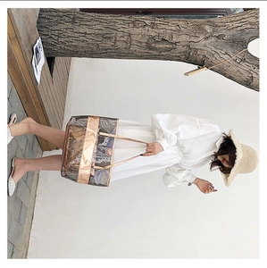 Detailed side view of a large transparent PVC tote bag with rose gold metallic leather trim