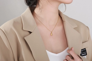 Gros plan d'un collier doré avec pendentif ovale porté par un mannequin en veste