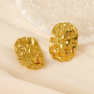 Detailed macro shot of gold oval earrings with woven texture on beige fabric background